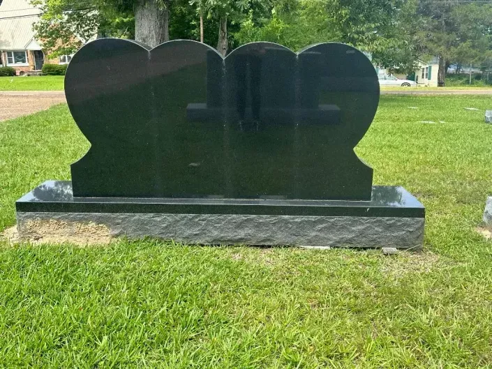 Black granite headstone in a grassy cemetery, with a rounded top and rectangular base.