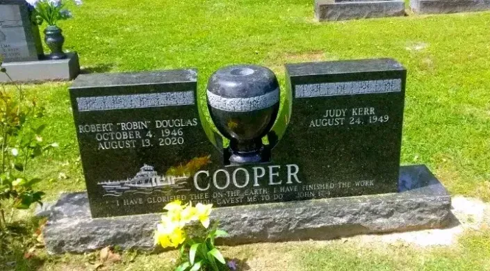 COOPER gravestone with flowers in a green cemetery, featuring two dark headstones and a round center marker