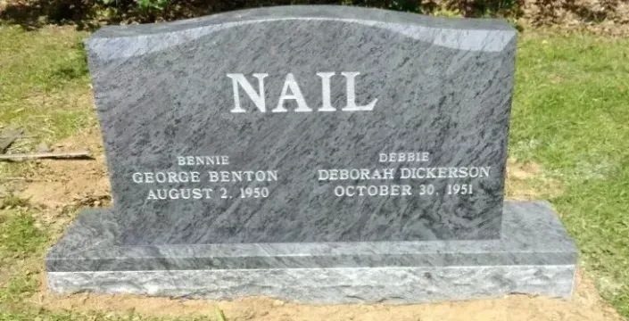 Gray granite headstone in a grassy cemetery, engraved “NAIL” with two names and dates.