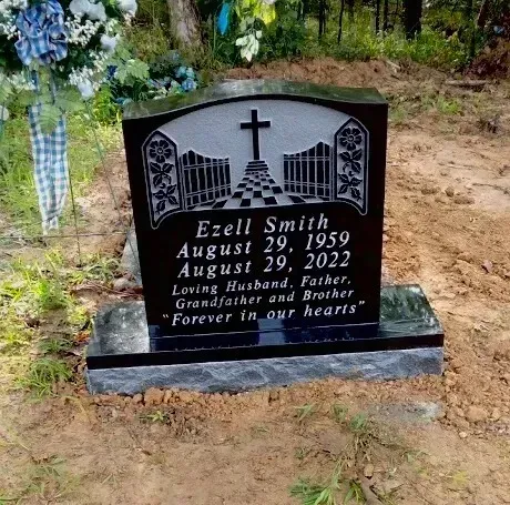 Black gravestone with cross and city skyline engraving in a wooded cemetery