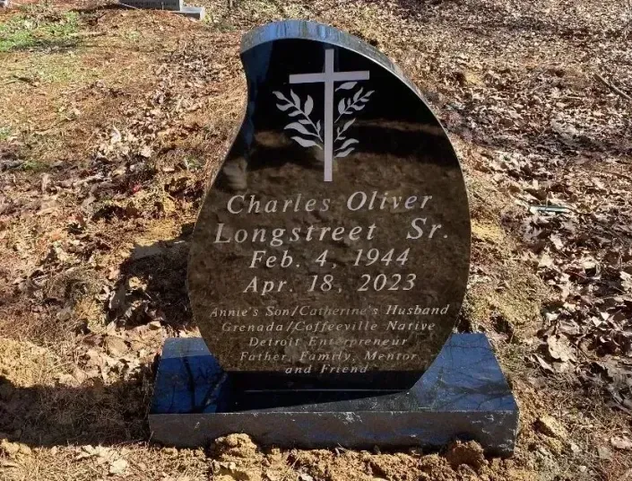 Black gravestone with cross in a wooded cemetery, engraved for Charles Oliver Longstreet, Feb. 4, 1944–Apr. 18, 2023