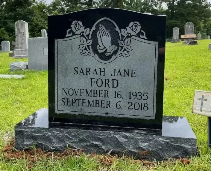 Black gravestone for Sarah Jane Ford in a grassy cemetery, with white engraved text and floral carving.