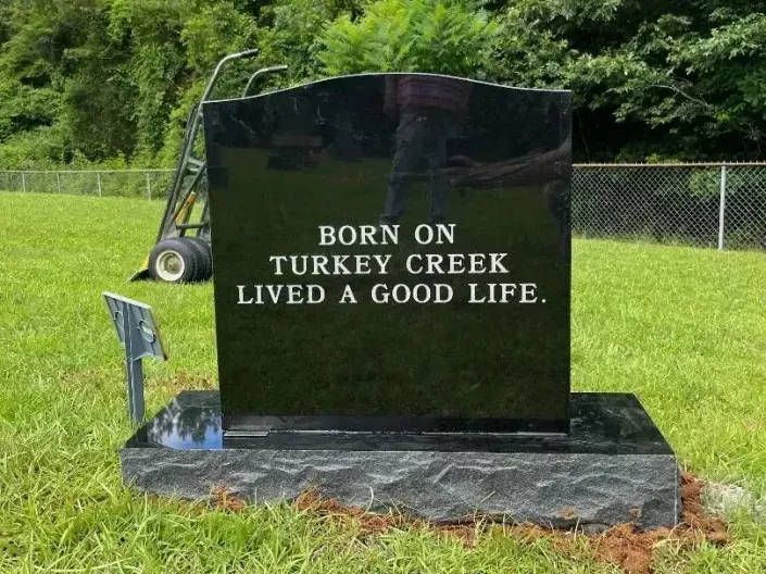Black granite memorial stone in a grassy cemetery reads “BORN ON TURKEY CREEK LIVED A GOOD LIFE.”