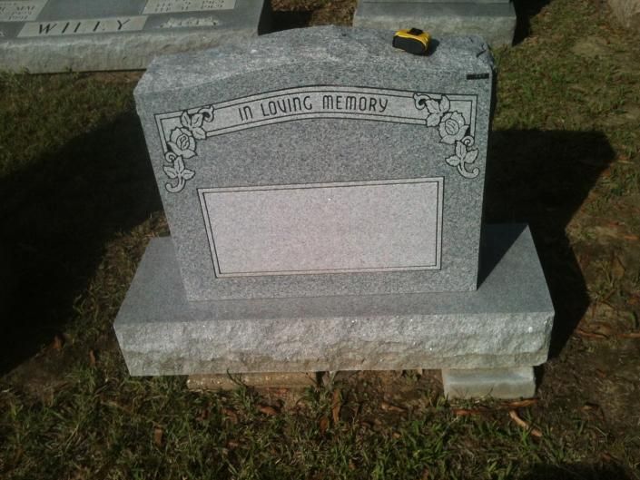 Gray memorial tombstone on a stone base in a grassy cemetery.