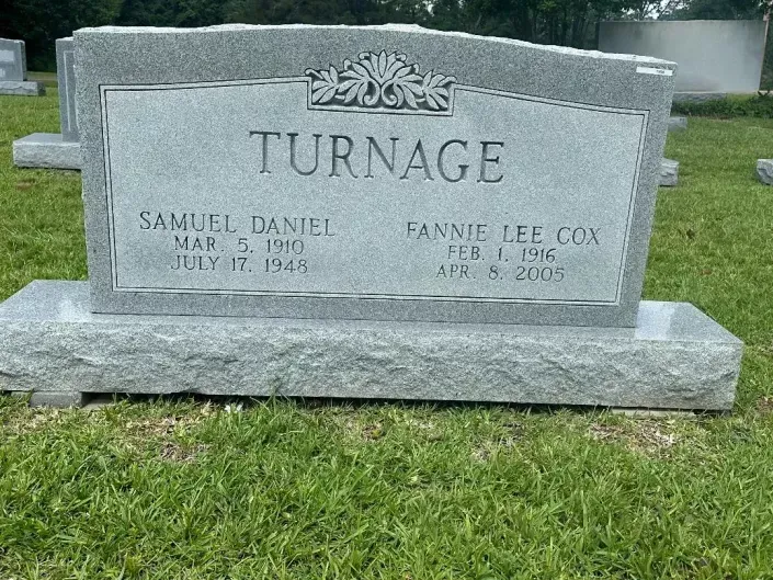 Gray granite grave marker with the name TURNAGE in a grassy cemetery
