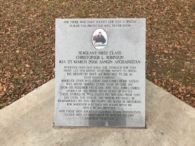 Stone memorial plaque on a concrete base surrounded by fallen leaves outdoors.