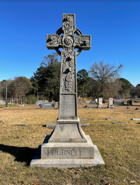 Tall stone cross monument in a cemetery under a clear blue sky