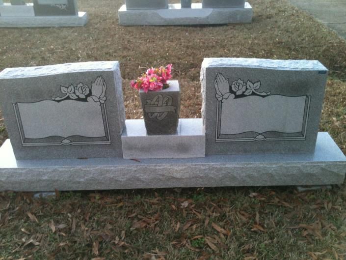 Gray granite double headstone with engraved plaques and a small flower vase in the center on a grassy cemetery plot