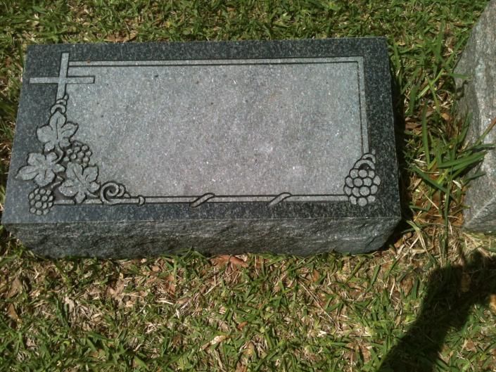Gray granite gravestone with floral and cross engraving in a grassy cemetery