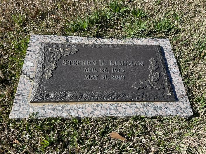 Gravestone set in grass with a dark plaque and stone border, engraved with a name and dates.