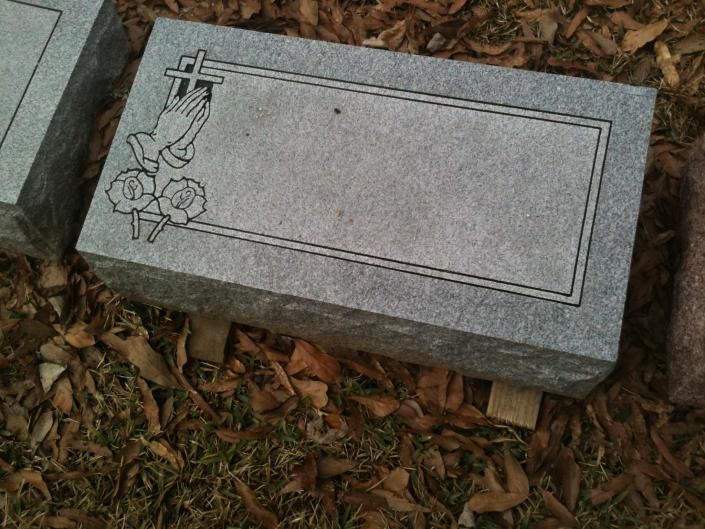 Gray gravestone with engraved cross and roses lying among fallen leaves