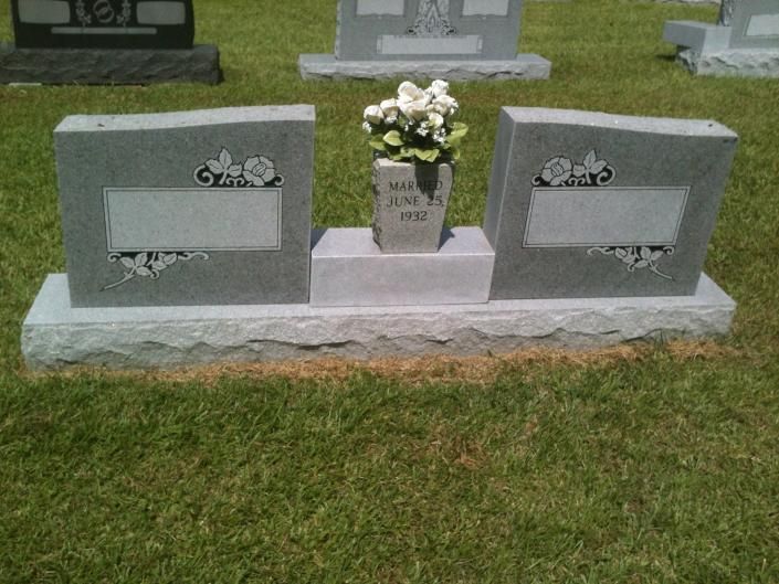 Granite cemetery memorial with two plaques and a vase of white flowers on a grassy plot