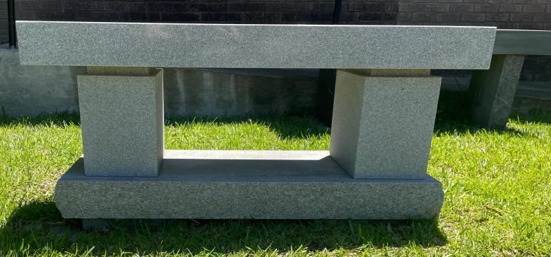Concrete bench in a sunny grassy area, with a dark wooden top and gray supports