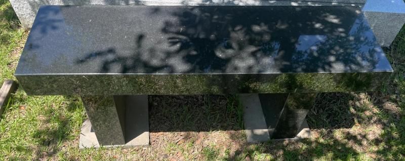 Black stone memorial bench on grass with sunlight and tree shadows