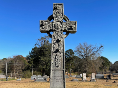 Stone Celtic cross monument in a cemetery under a bright blue sky
