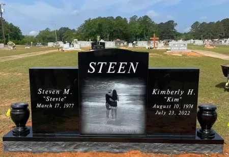 Black granite cemetery headstone with STEEN, engraved portrait, and engraved names on a sunny lawn.