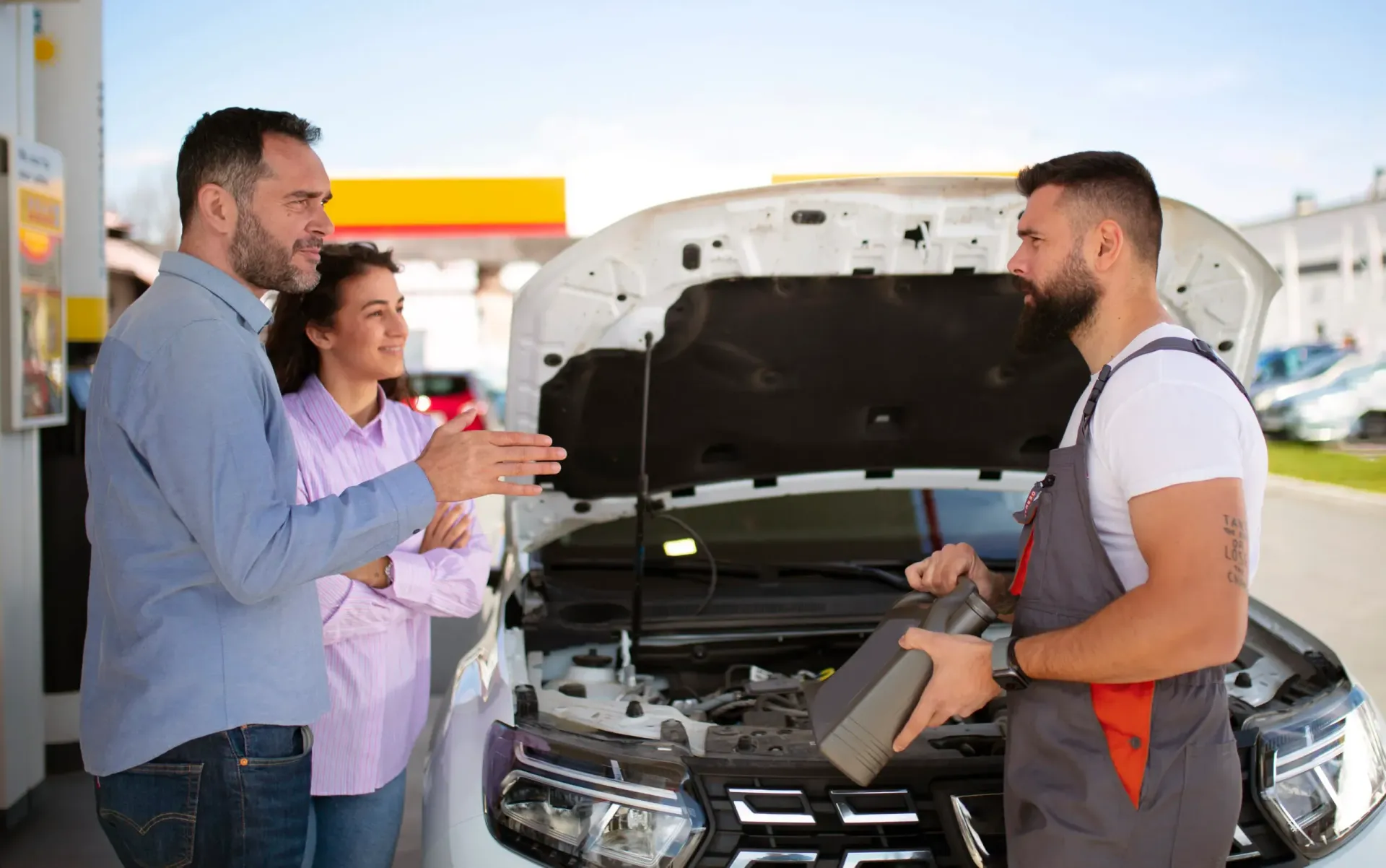 Three people discussing a car repair with the hood open at an auto shop