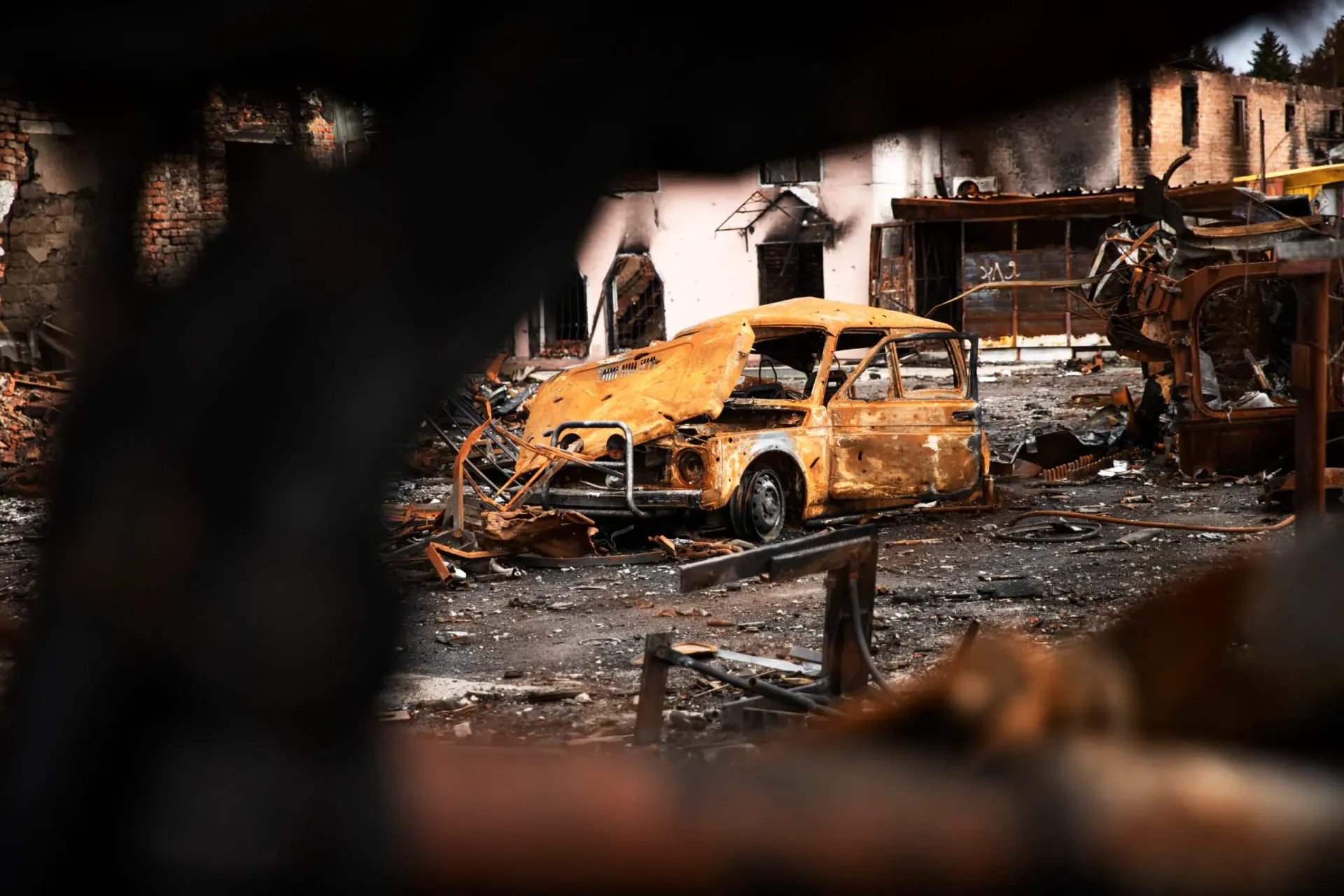 Burned-out yellow car amid fire-damaged debris in a destroyed street scene