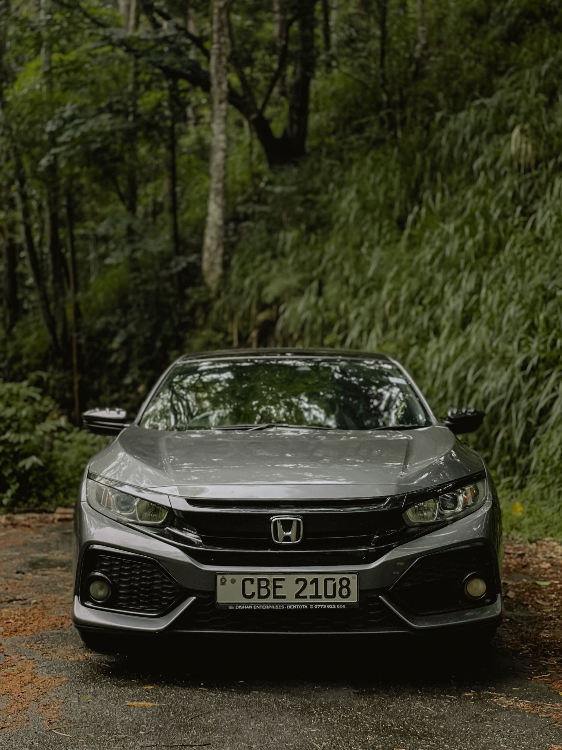 Silver Honda sedan on a narrow forest road, front view with license plate CBE 2108.
