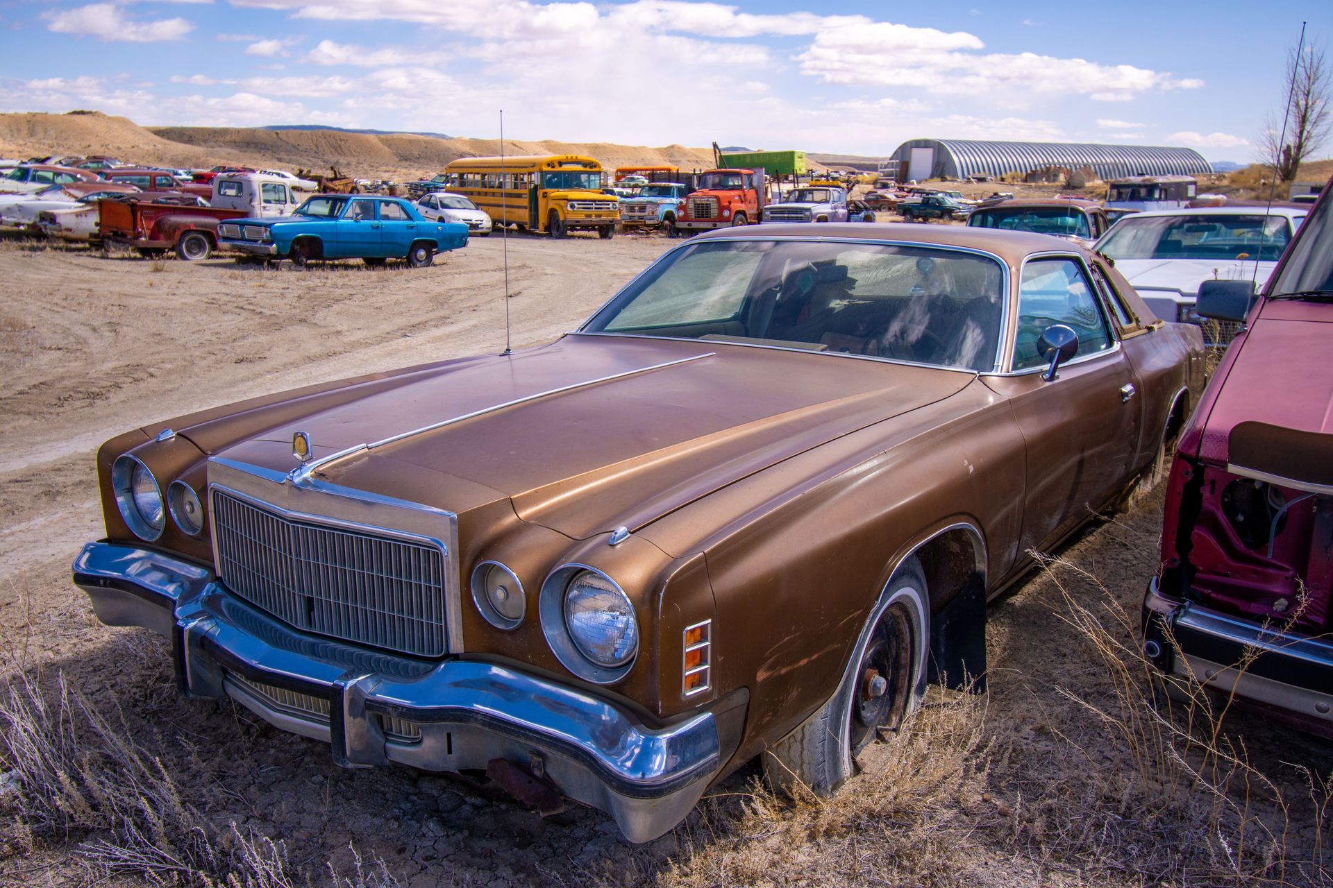Brown vintage car parked in a dusty lot with other classic cars in the background