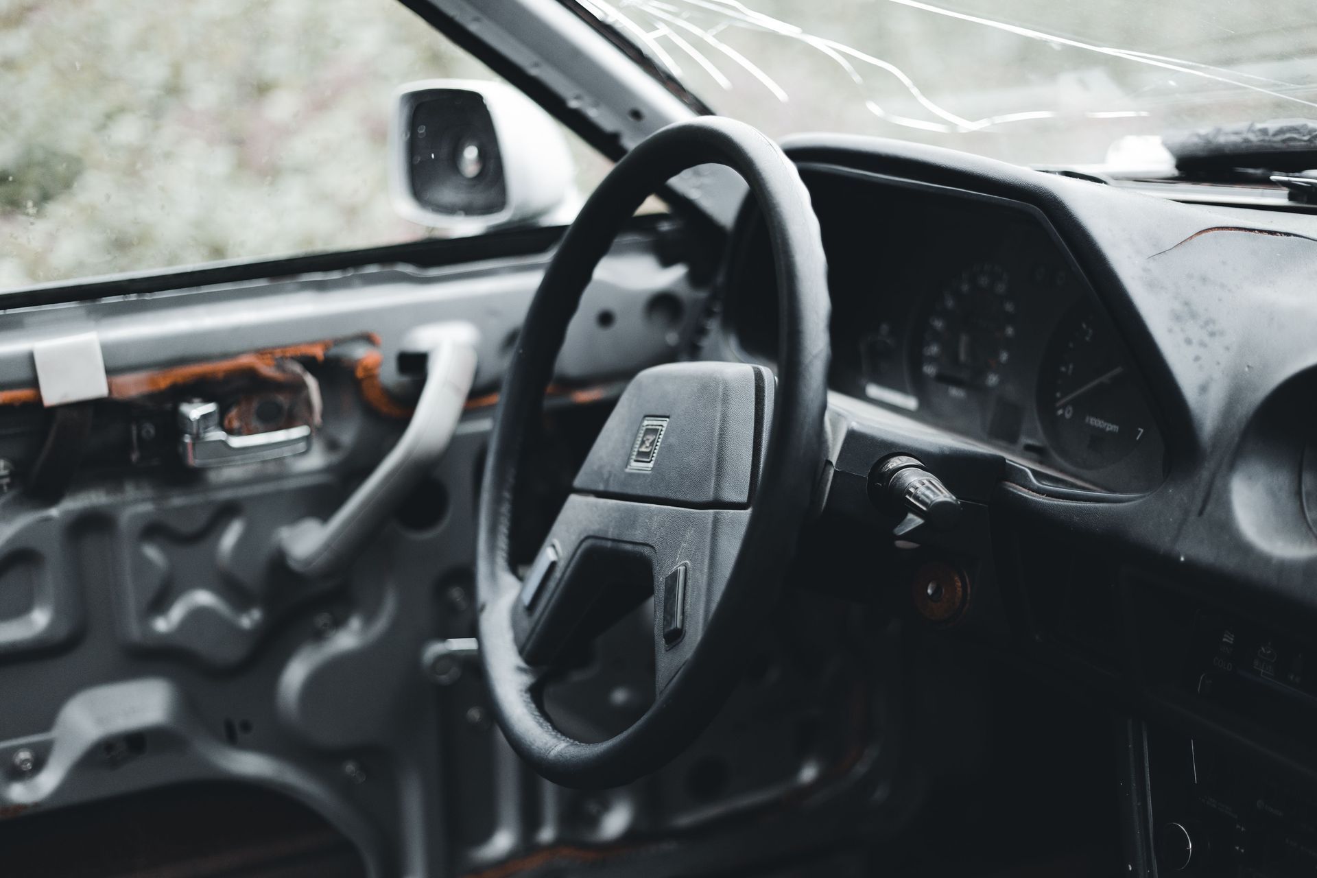 Damaged car interior with steering wheel and cracked windshield, water leaking inside