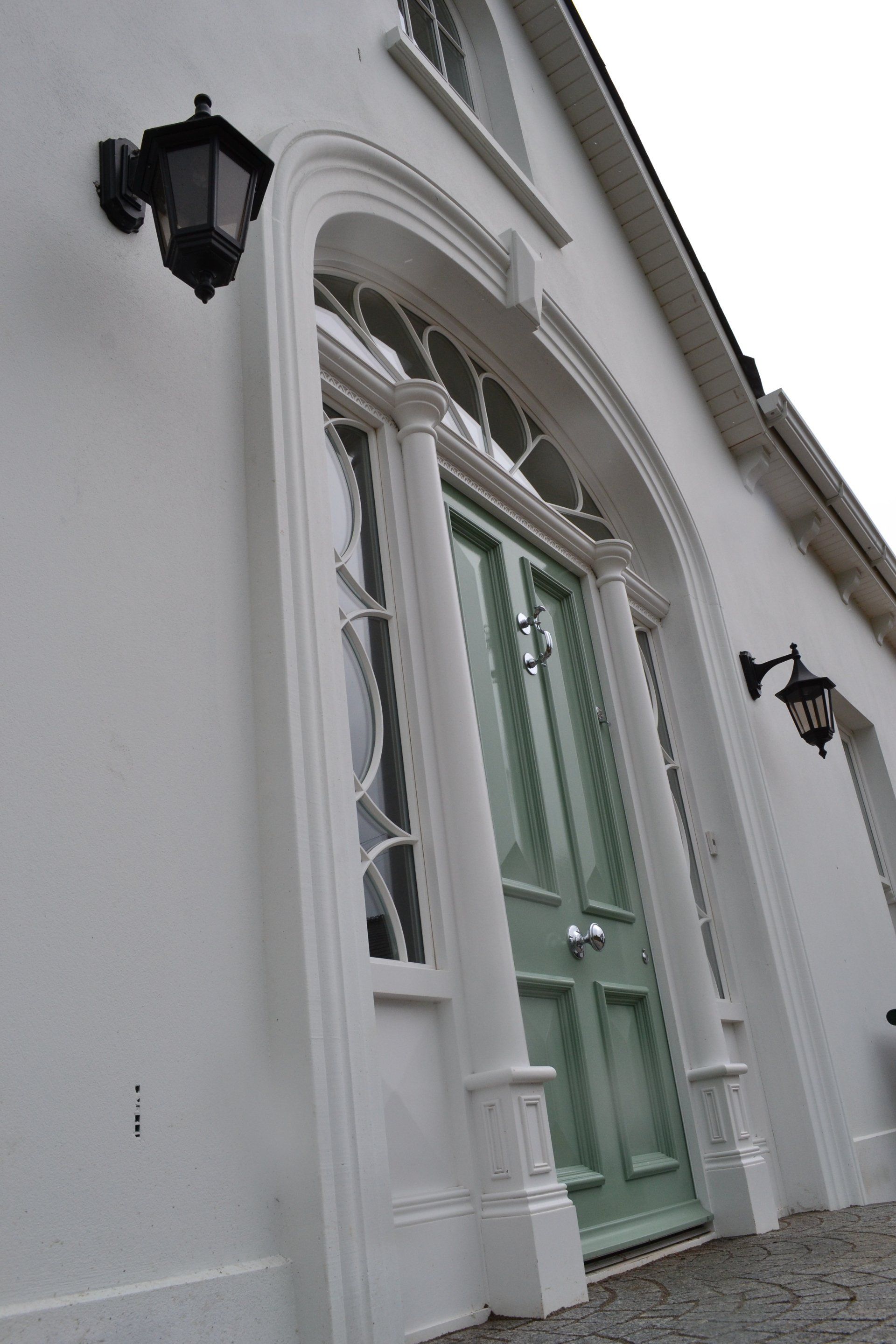 A white building with a green door and two lights on the side.