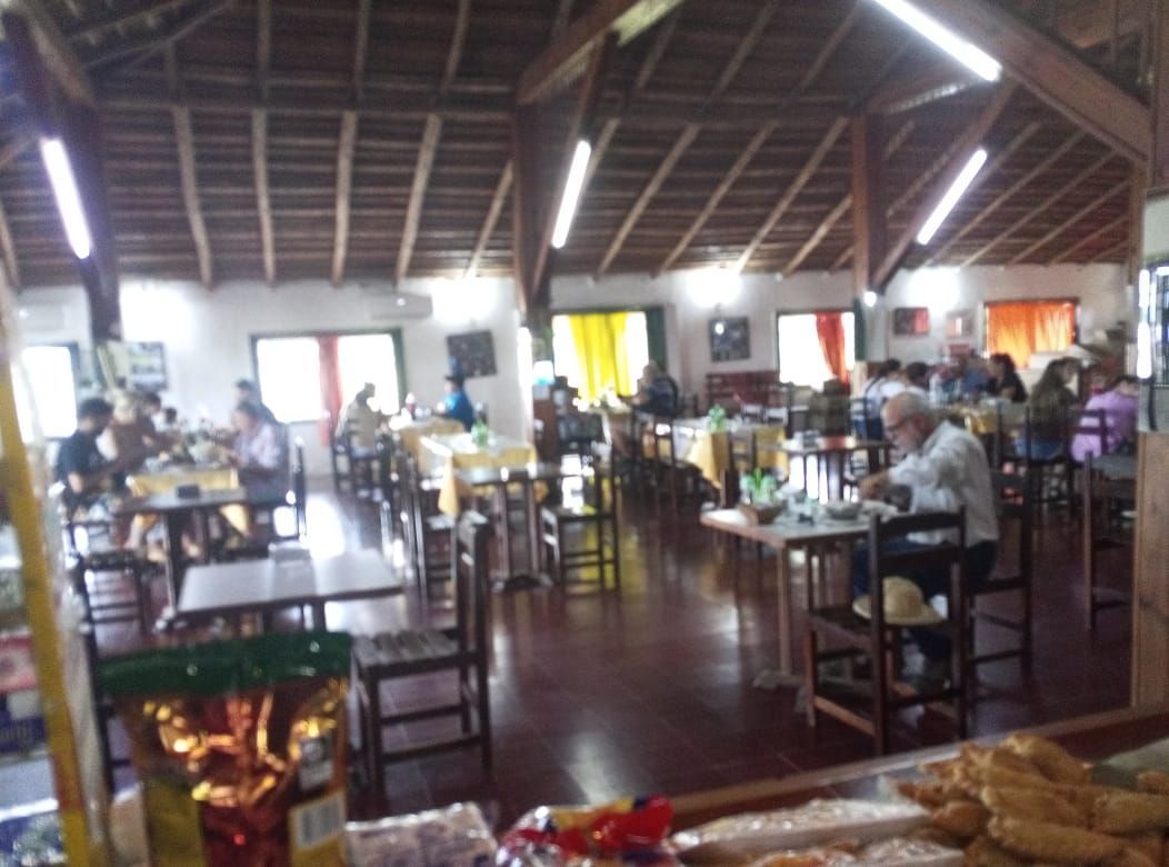 Interior de restaurante con techo de madera, mesas, sillas y gente cenando.