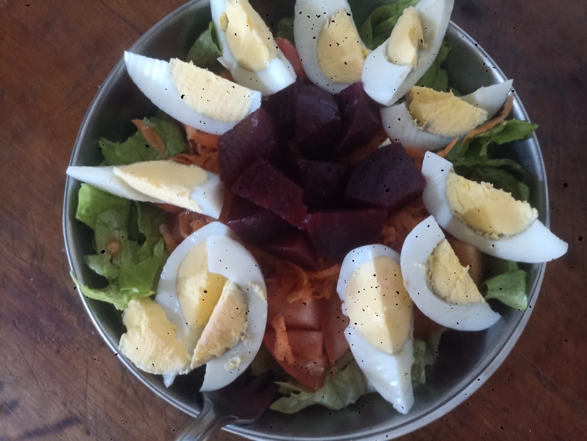Ensalada en recipiente de metal: lechuga, huevos cocidos en rodajas, remolacha, zanahorias; espolvoreado con pimienta.