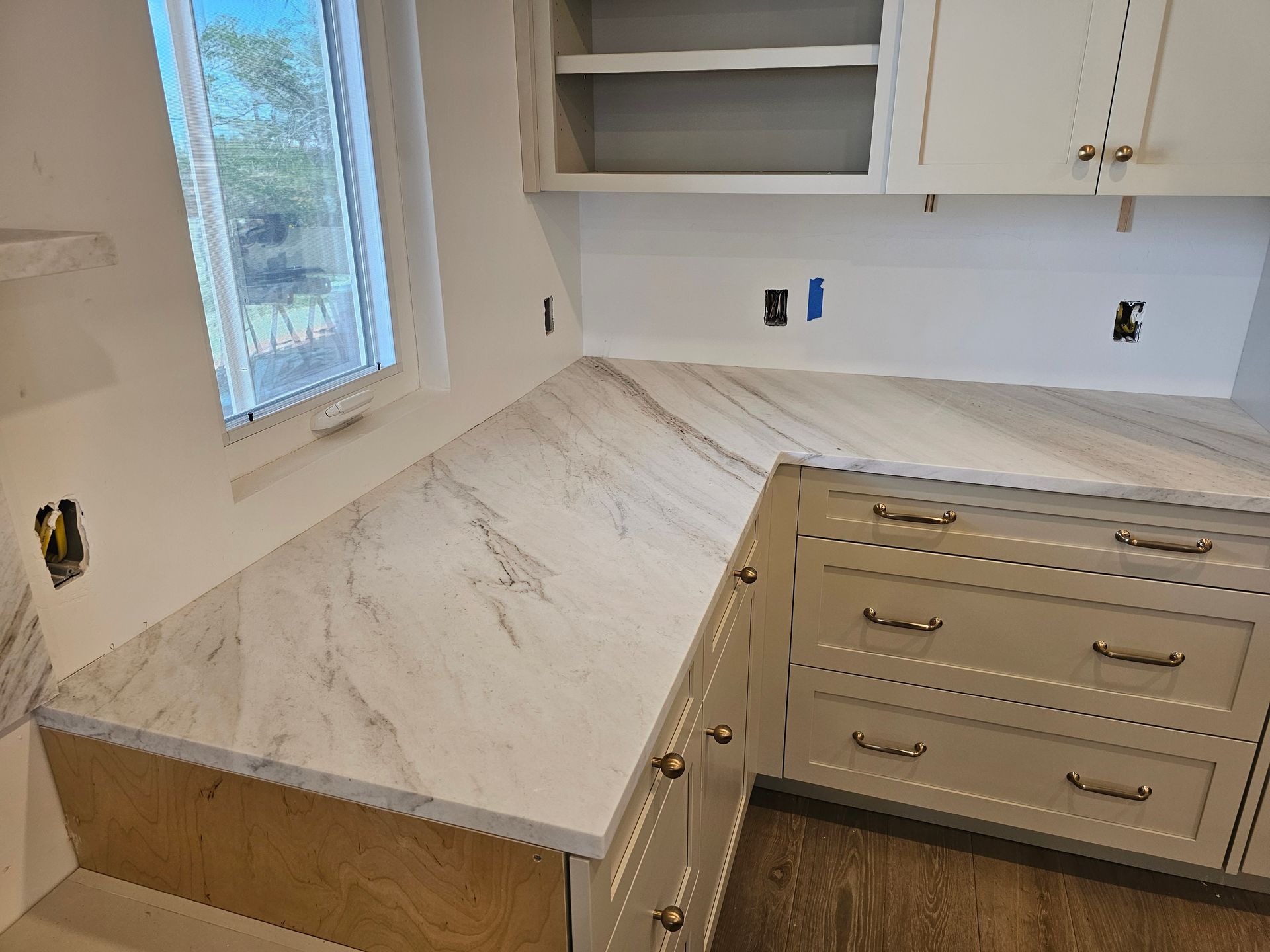 Corner kitchen with white cabinets, marble countertop, and a window.