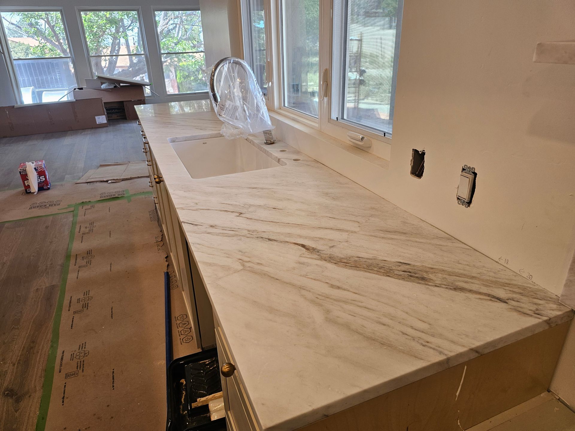 White marble countertop with gray veining; sink, faucet, and windows in the background.