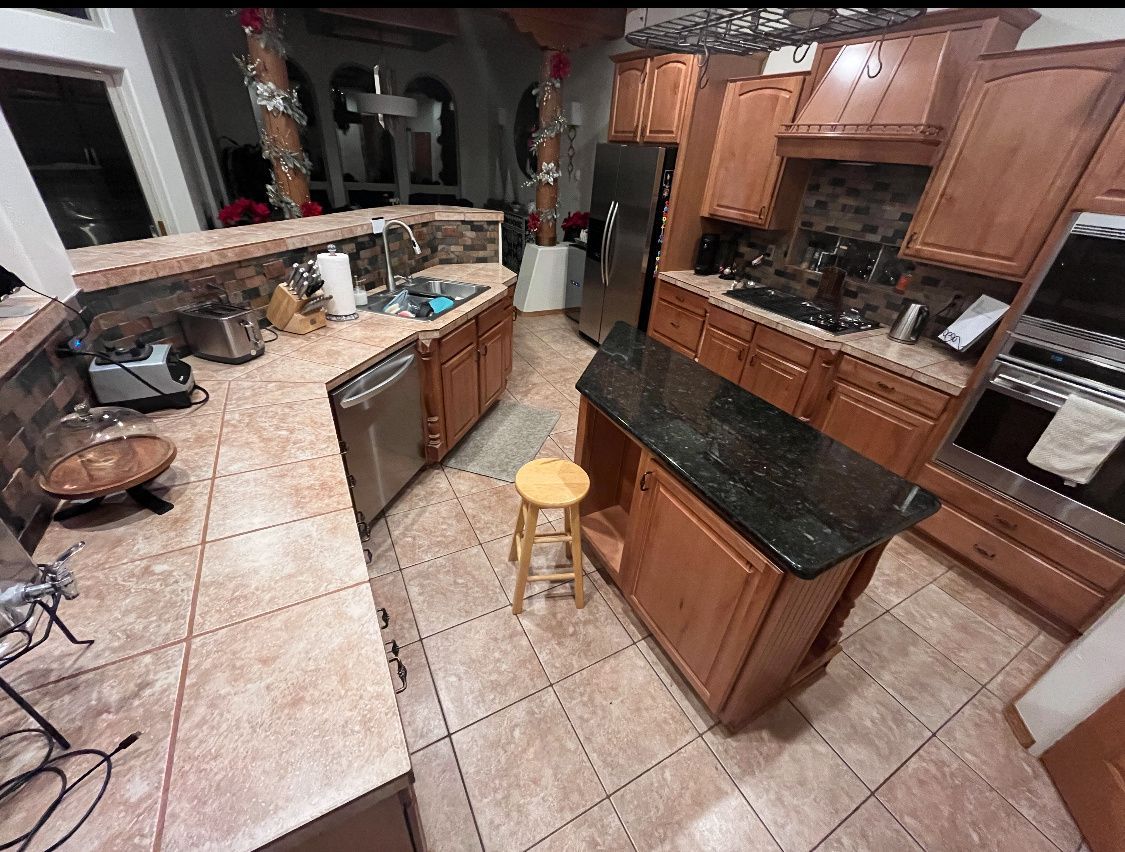 Kitchen with brown cabinets, black countertops, and a center island with a stool.