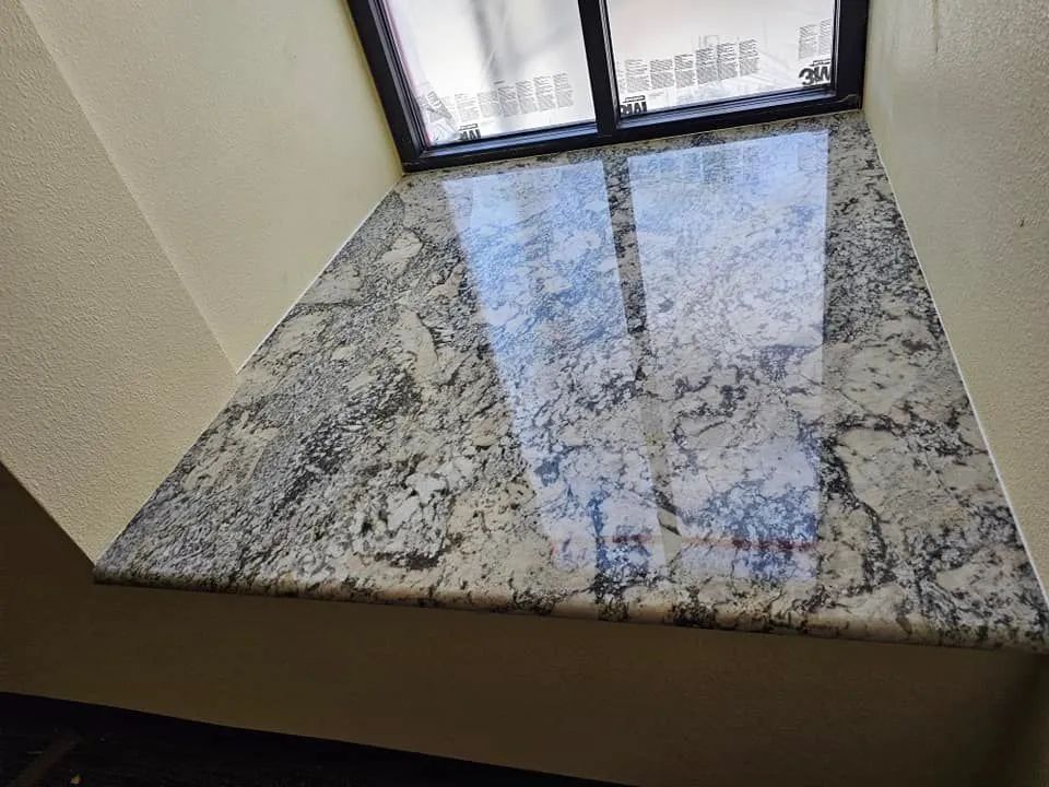 A window sill with a granite counter top in front of a window.