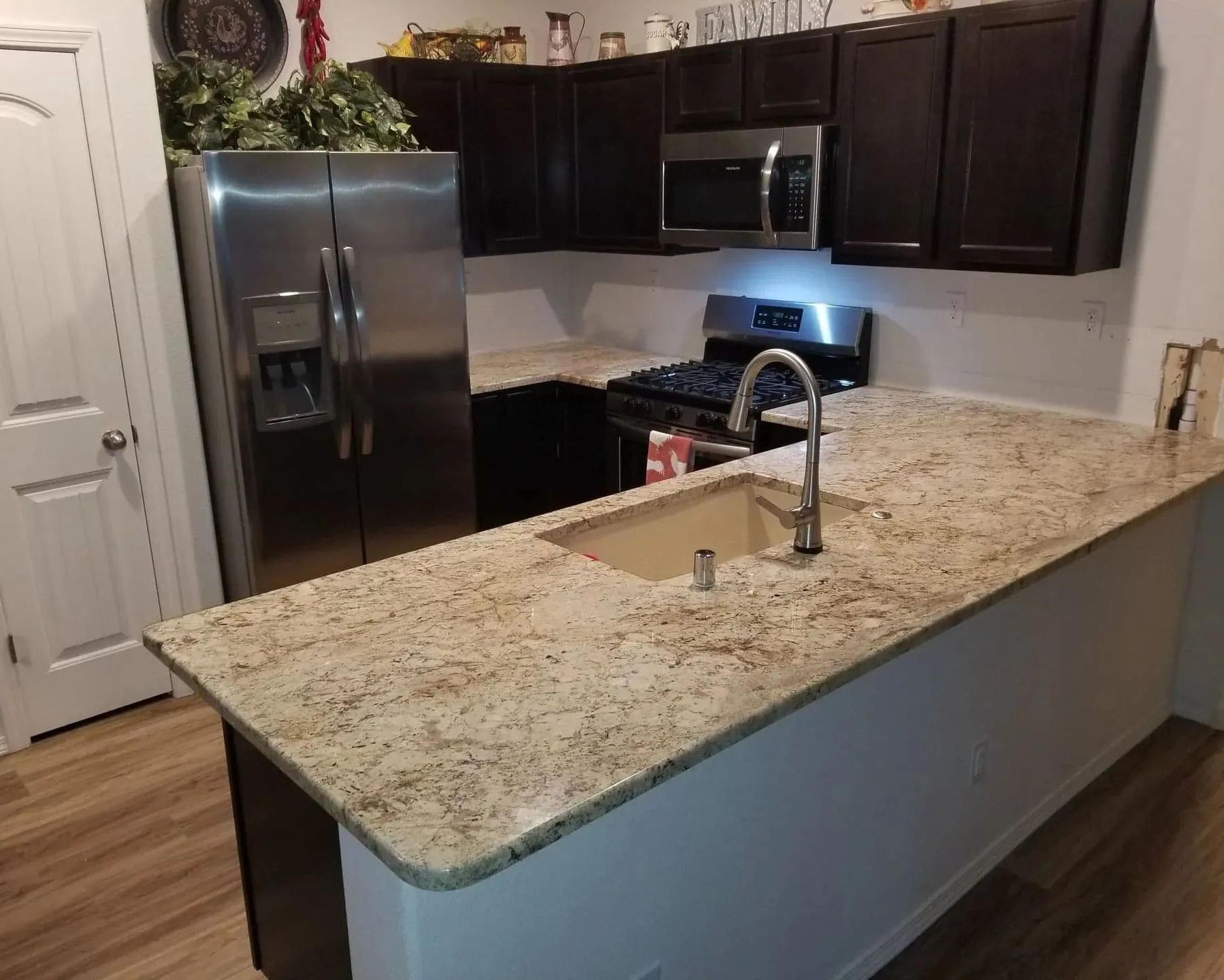 Modern kitchen with dark cabinets, stainless appliances, and a large granite island with sink and faucet
