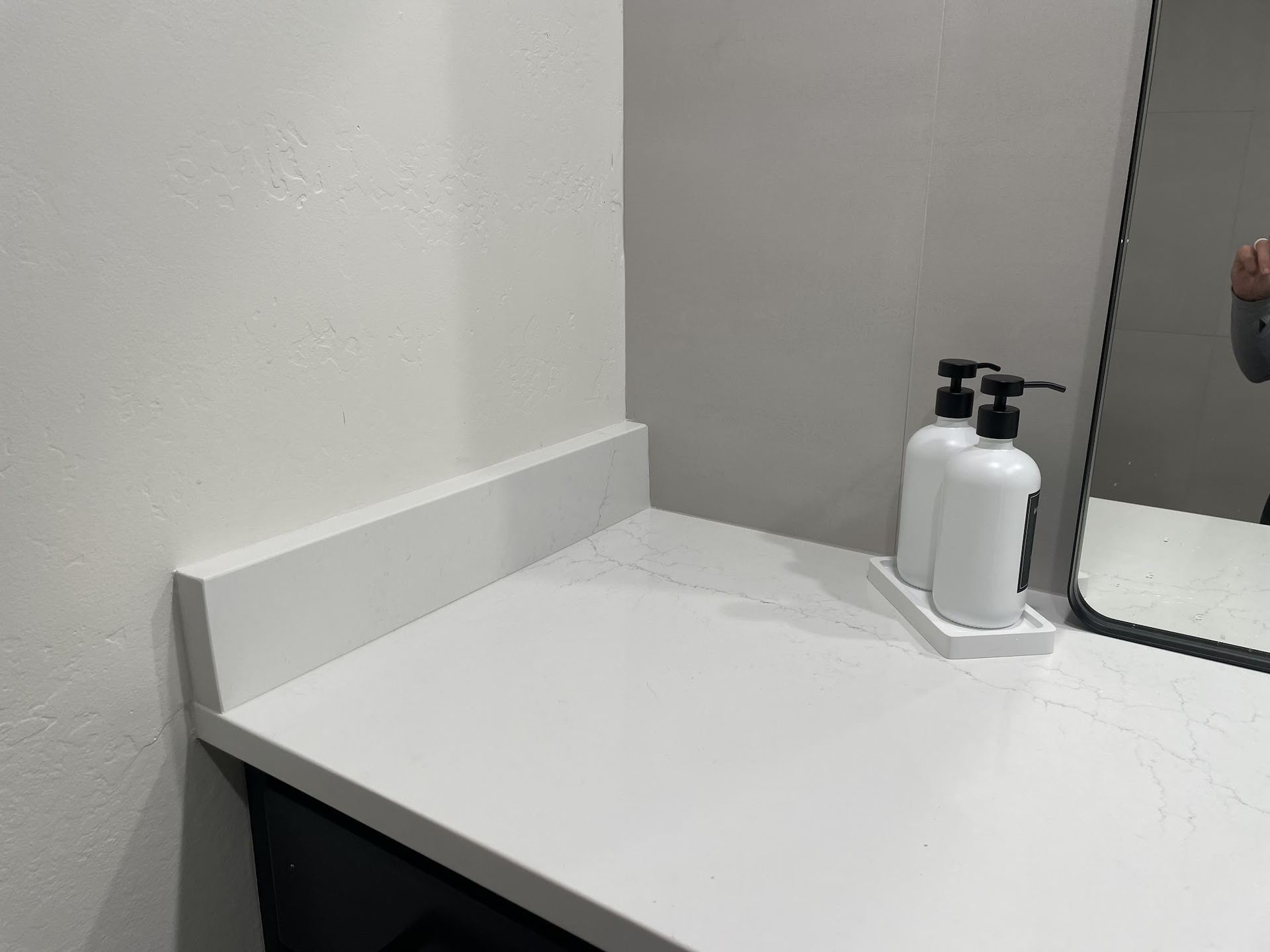 White countertop with soap dispensers, next to a mirror in a bathroom.