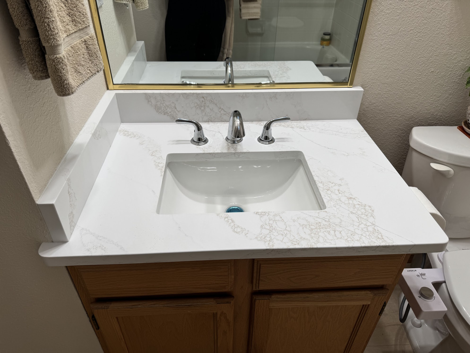 Bathroom vanity with white countertop, sink, faucet, wooden cabinet, and toilet on the right.