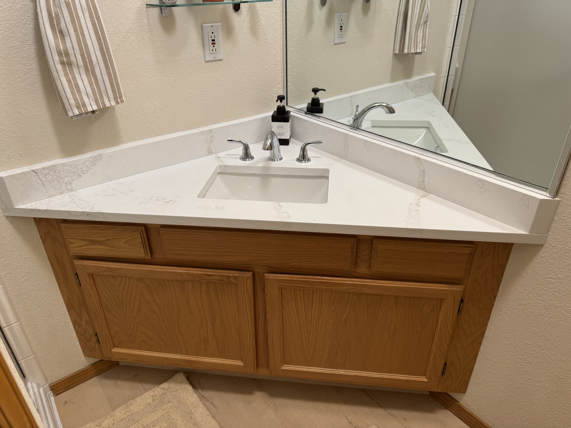 Bathroom vanity with a triangular countertop, oak cabinet, and a rectangular sink.