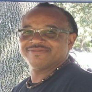 A man wearing glasses and a necklace is smiling for the camera.