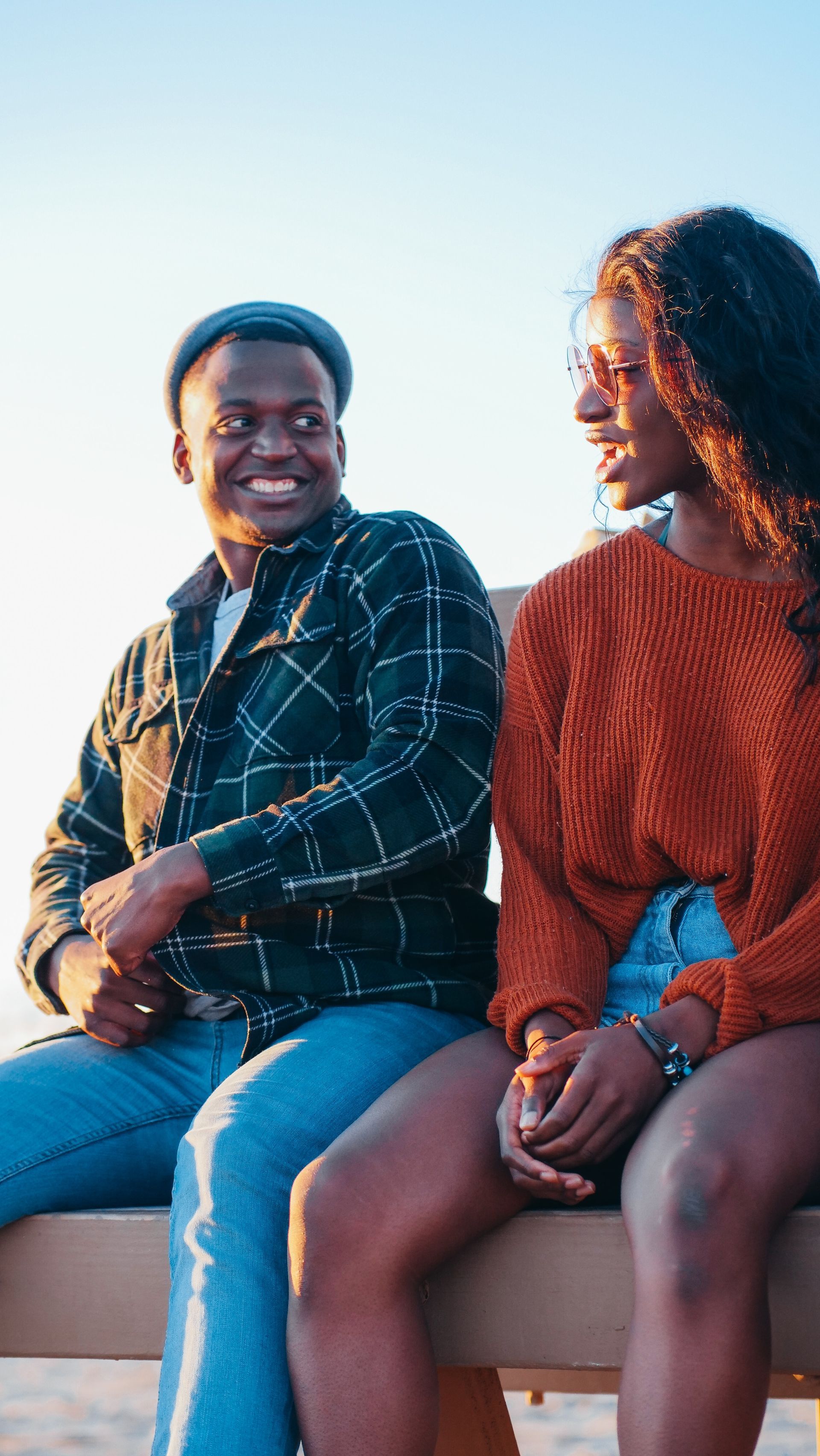 A man and a woman are sitting on a bench talking to each other.