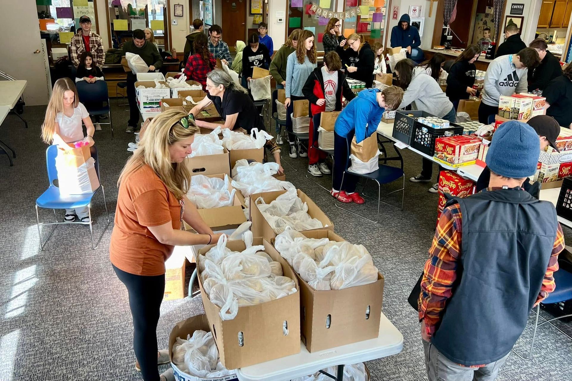 People packing bags at tables, likely a food drive or donation event, indoors.