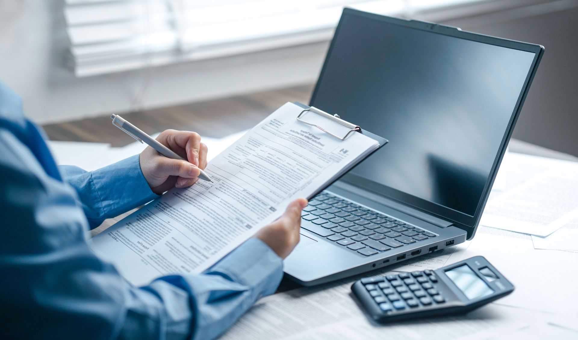 Person reviewing paperwork beside a laptop and calculator.