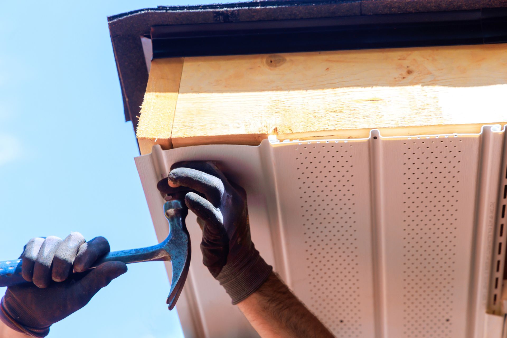 A worker installs roof flashing while standing on a ladder in a residential area. A worker installs roof flashing while standing on a ladder in a residential area.