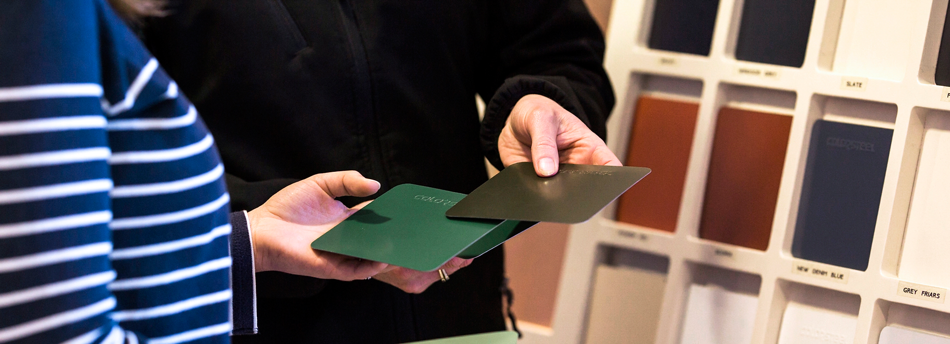 Person holding two green folders in front of a wall of color swatches