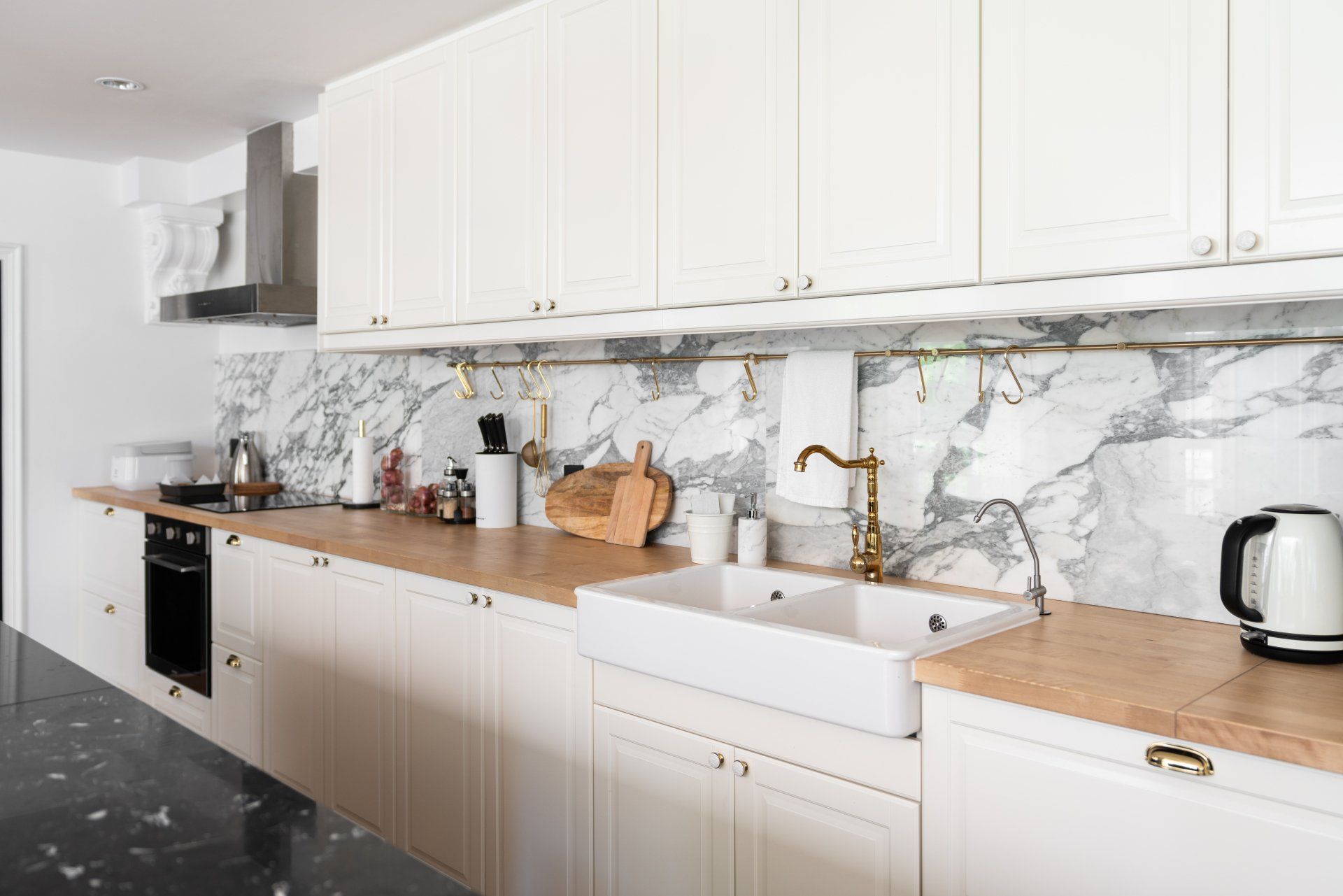 Modern white kitchen with wooden countertops, brass fixtures, marble backsplash, and farmhouse sink