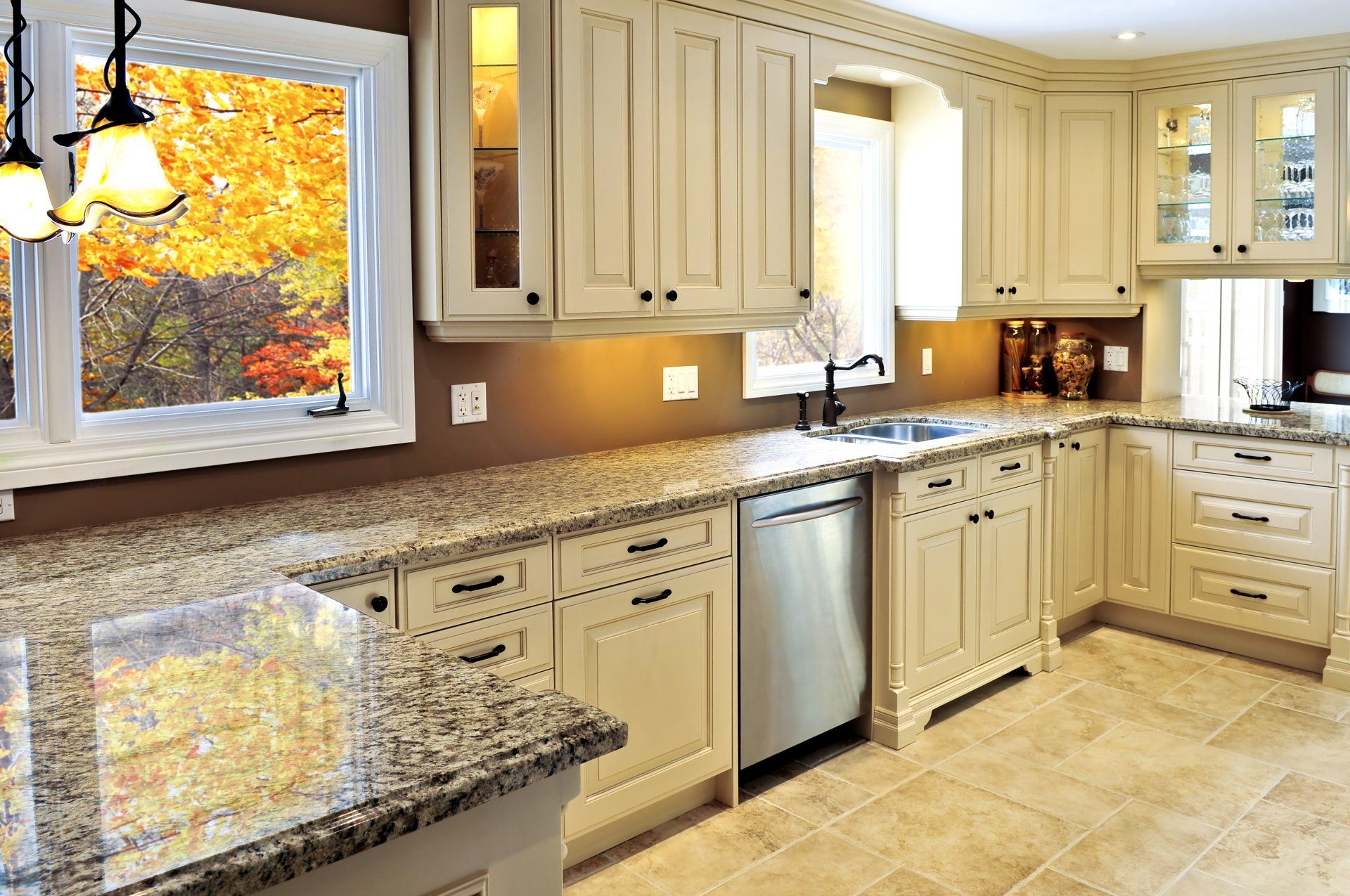 Bright modern kitchen with cream cabinets, granite countertops, and a large window showing autumn trees.