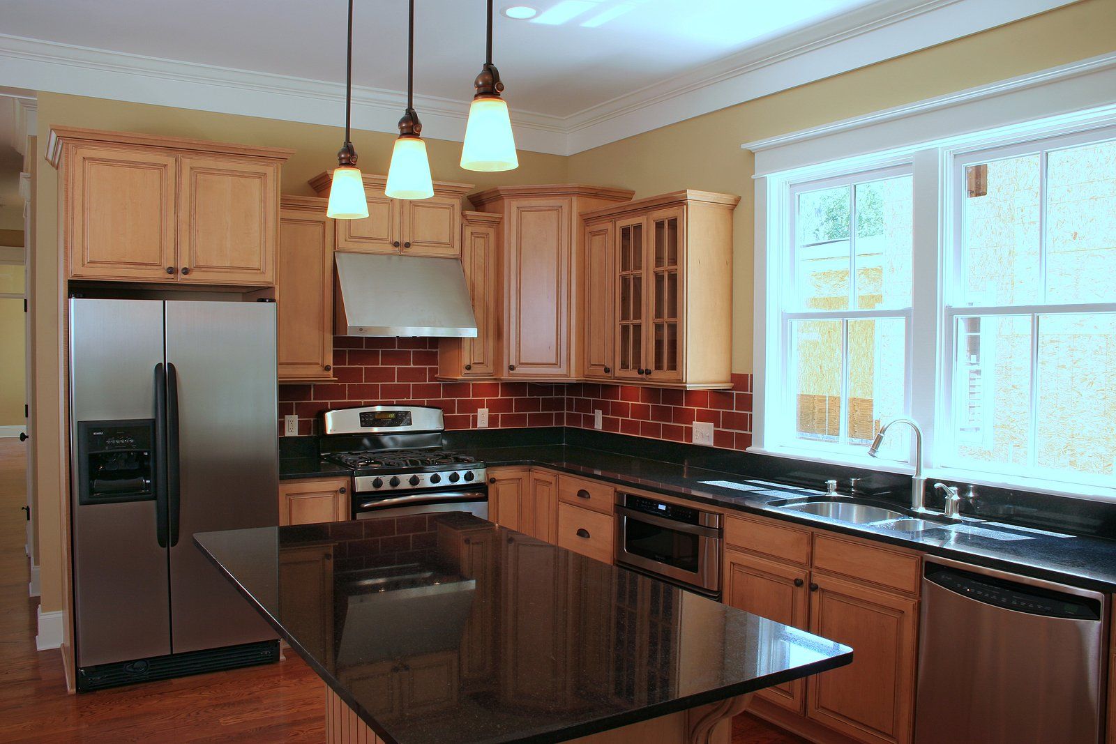 Modern kitchen with stainless steel appliances, dark counters, wood cabinets, and pendant lights