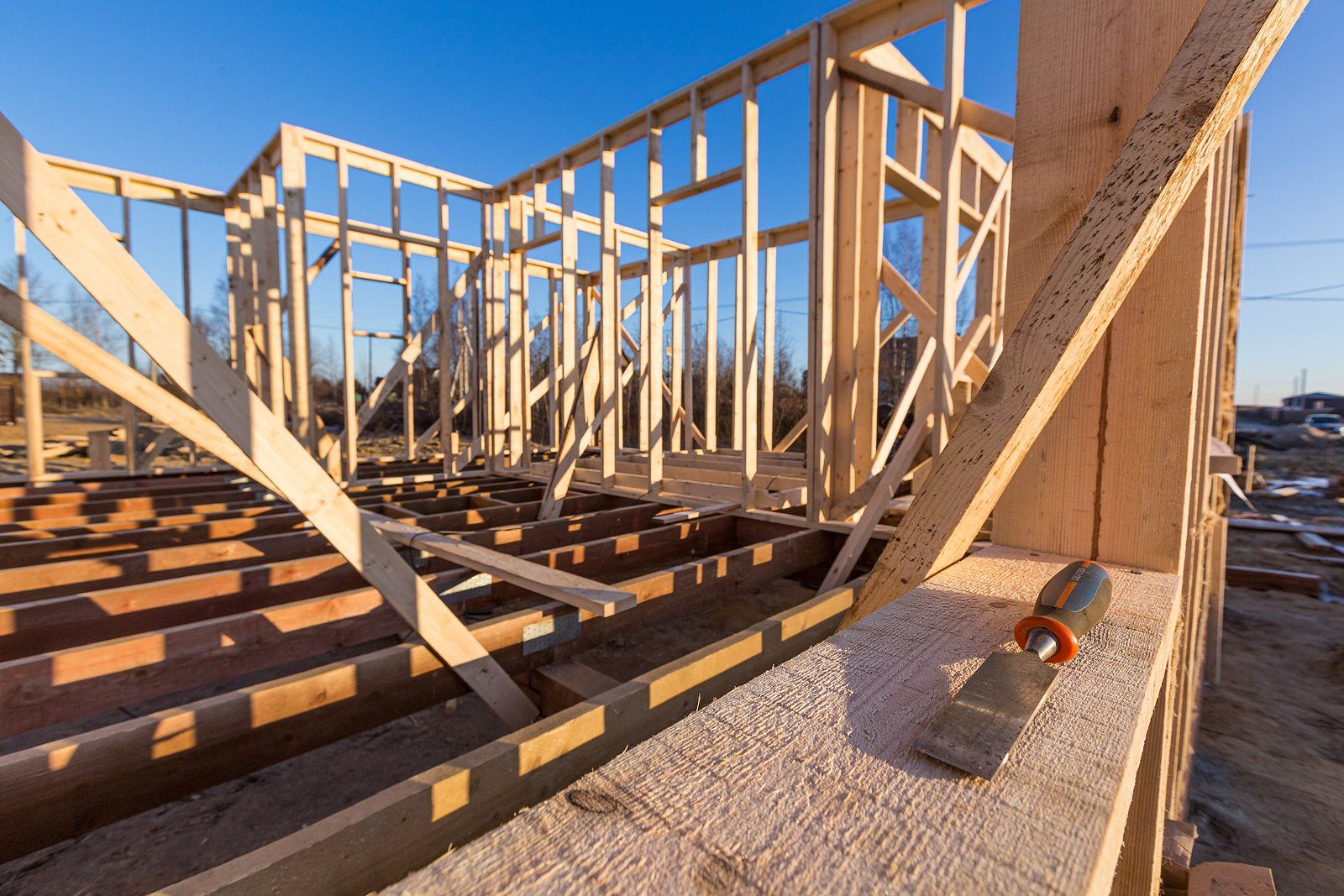 Framed house under construction with exposed wooden beams and floor joists in bright sunlight