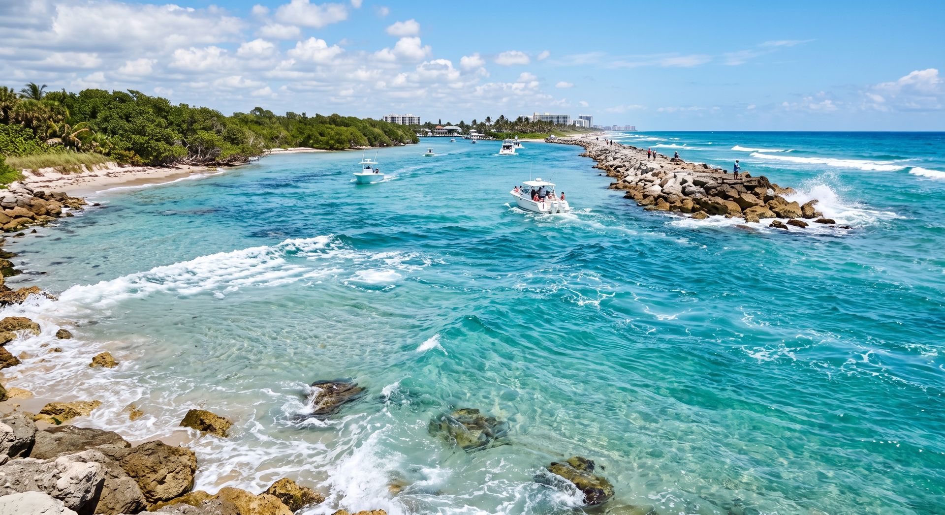 Turquoise ocean cove with rocky breakwater, small boats, and a sandy beach under a bright blue sky