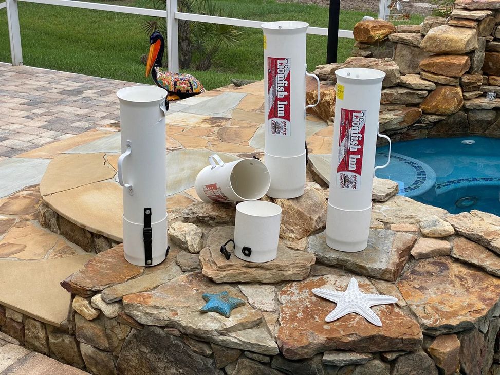 White pool cleaner cylinders with handles sit on a stone ledge near a pool, with one open.