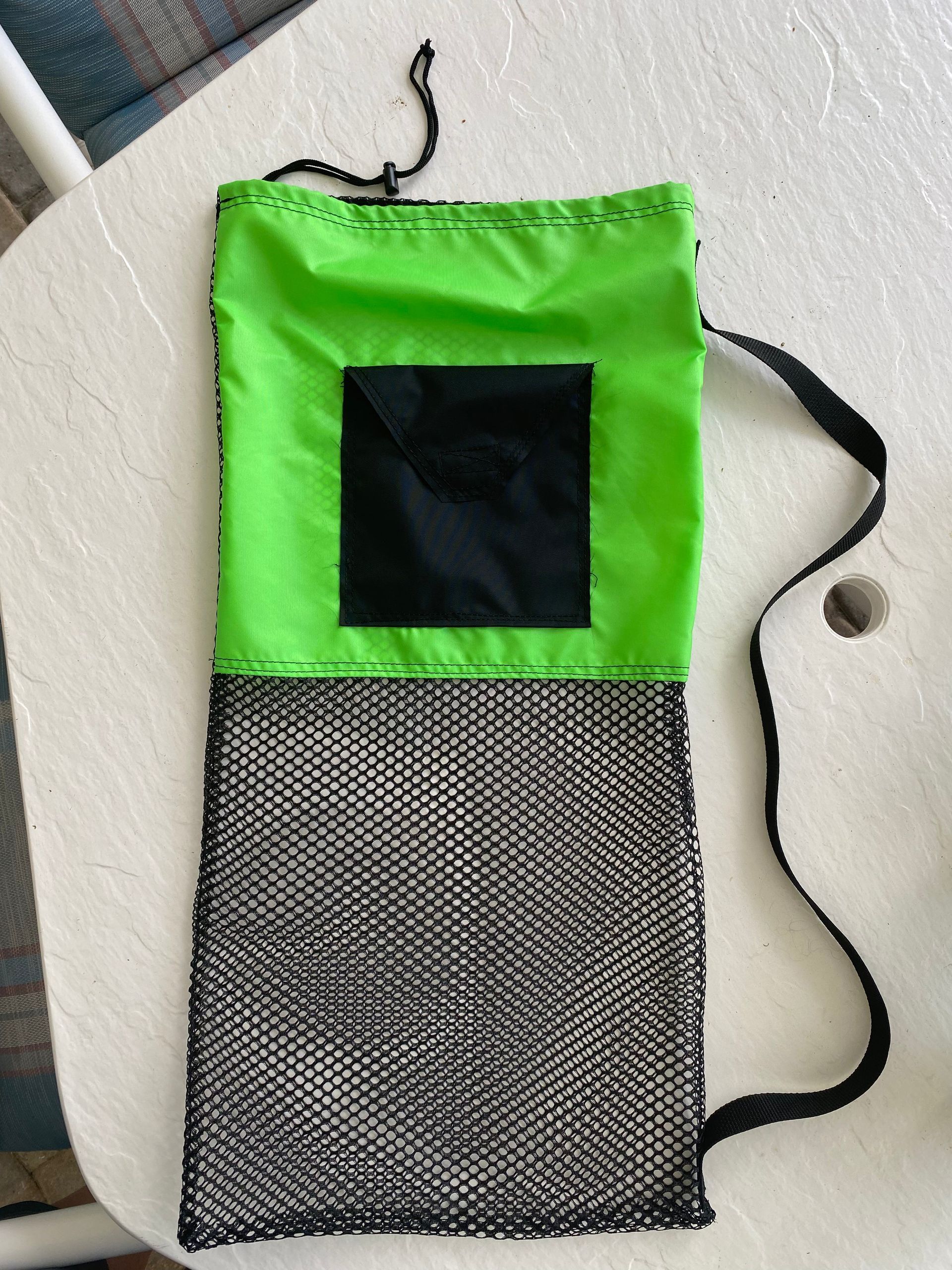 Green and black mesh bag with a drawstring, black strap, and black square on the top.