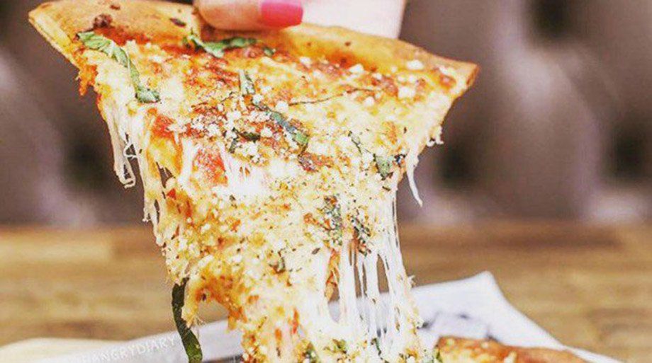 Slice of pizza being lifted, showcasing melted cheese and basil on a wooden table.